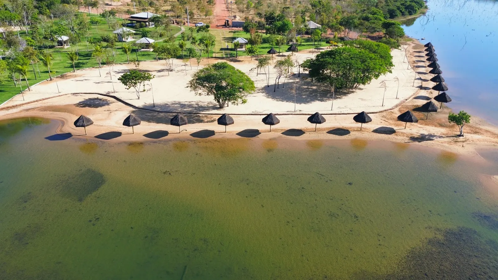 Faixa de areia do Quinta do Lago vista do alto, com uma fileira de quiosques de palha na beira da água e o gramado atrás